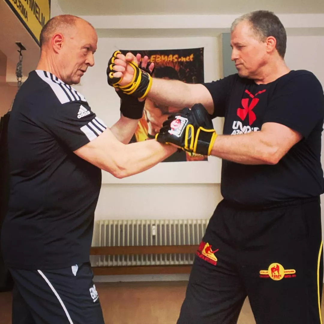 A middle-aged adult in casual athletic wear practicing a Wing Chun stance with a calm, focused instructor in a clean, minimalist martial arts studio, soft natural side lighting, wide shot, realistic, documentary style, no text.